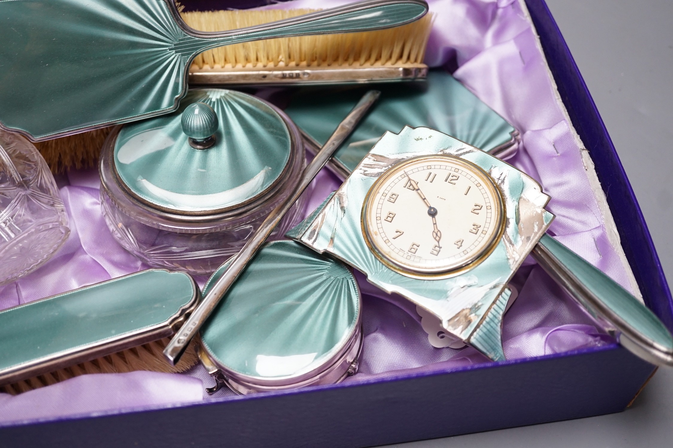 A George V silver and green guilloche enamel set nine piece dressing table set, by Albert Carter, Birmingham, 1933/4, together with a similar unmarked timepiece, comb teeth missing and enamel a.f.
